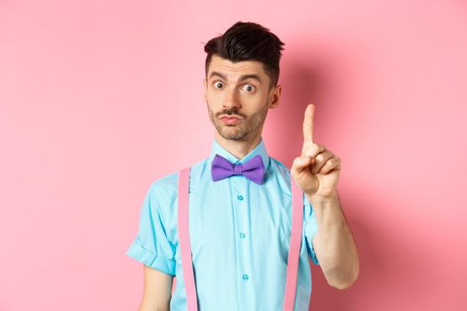 Young funny guy showing finger to explain something, prohibit or warn you, standing on pink background. Copy space