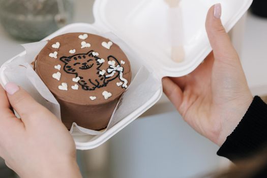 Woman hold bento cake with cupe picture of cat and white sugar hearts in eco box-packaging with wooden spoon.