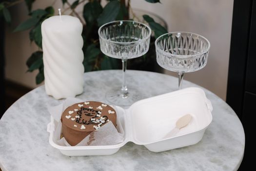 Chocolate bento cake with white candle and chmpagne glasses on luzury marble table.