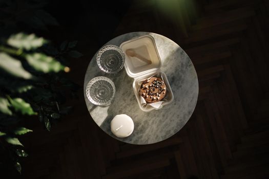 Top view of Chocolate bento cake in eco box with wooden spoon. White candle and chmpagne glasses on luzury marble table.