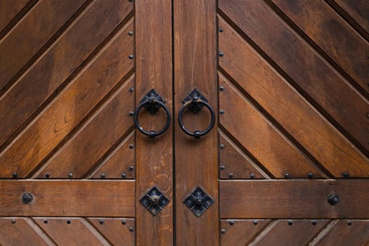 Brown wooden entrance with antique door ring handle. Details of ornate chocolate colour painted door. Vintage iron door knob. Classic style with straight lines