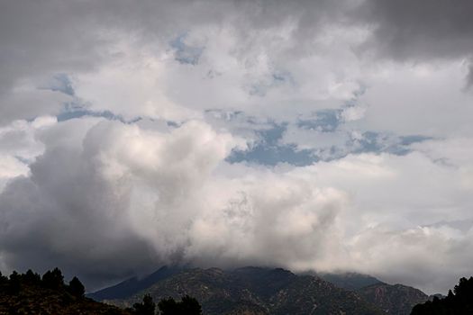 Mountain surrounded by large storm clouds. Trees, white and grey walnuts