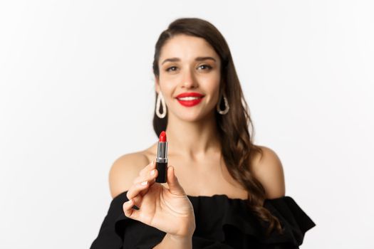 Fashion and beauty concept. Beautiful woman in black dress showing red lipstick and smiling, standing over white background.