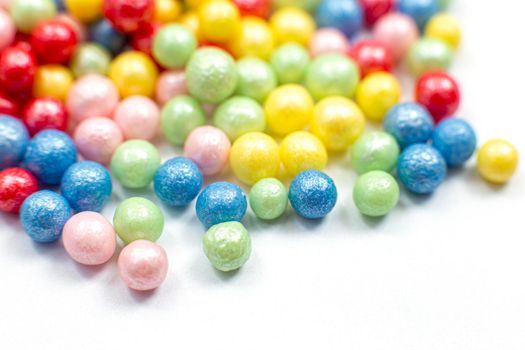 Multi-colored shiny spheres, sugar confectionery sprinkles, are scattered on a white background. Close-up