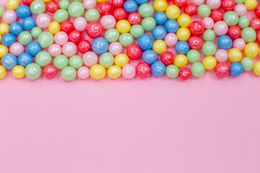 Multi-colored round glossy balls of sugar confectionery topping lie at the top on a pink background.Copy space