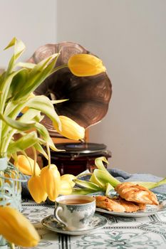 retro still life, sweet puff, tea in a vintage porcelain cup and a stack of books, a bouquet of yellow withering tulips in a vase,. High quality photo