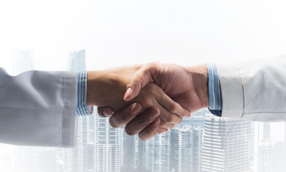 Close-up of the handshake between the two medics. Against the backdrop of the cityscape