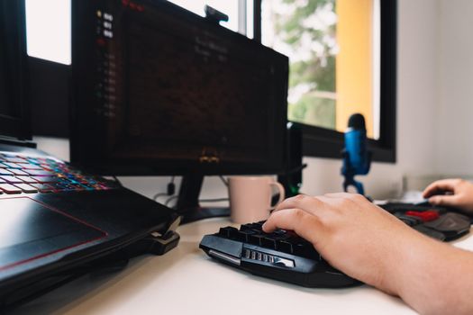 detail of a young man's hands using laptop keyboard works as a programmer from home. Natural light from desk window, with computer screen keyboard and coloured lights. Horizontal