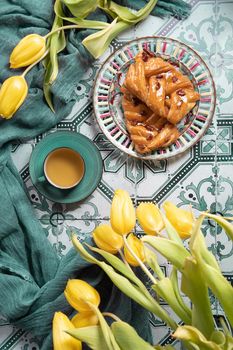 flat lay food, sweet puff, tea in a vintage porcelain cup and a stack of books, a bouquet of yellow withering tulips in a vase,. High quality photo