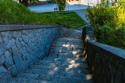 Stony stairs with green grass and bushes around and sunlight from space between tree leaves