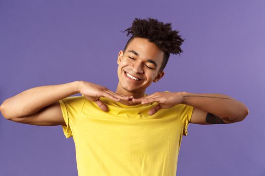 Close-up portrait of carefree handsome young man, do stretching exercises at home while on quarantine, hold hands sideways close eyes and tilt head dreamy, just woke up, purple background.