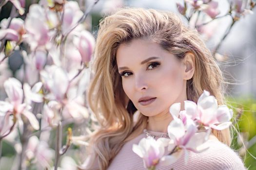 Portrait of a beautiful happy middle aged woman enjoying the smell in a blooming spring garden. Beautiful magnolia bushes, large flowers