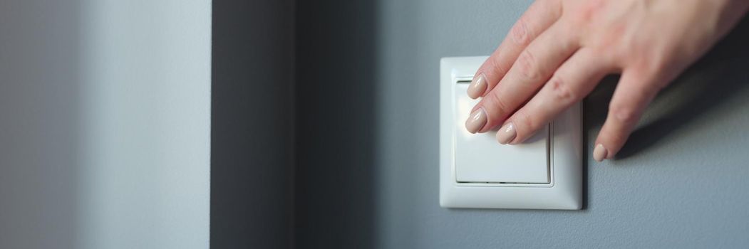 Female hand pressing light switch in apartment closeup. Energy savings concept