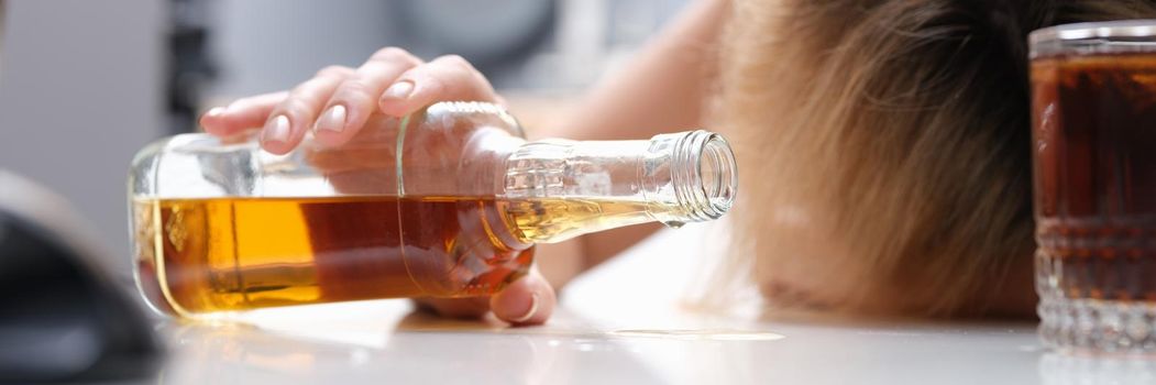 Woman sleeping at table with bottle of alcohol in her hands closeup. Alcohol addiction in women concept