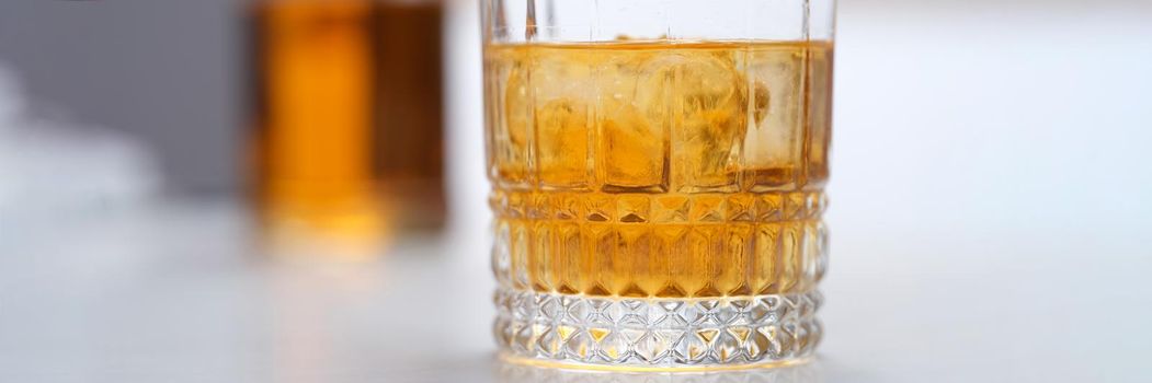 Glass of whiskey with ice standing on table closeup. Alcohol addiction treatment concept