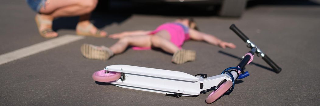 Little girl lies motionless on asphalt with scooter after collision with car.