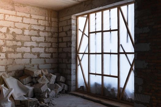 An unfinished room of a private house closed with an opaque film. Construction debris from aerated concrete.