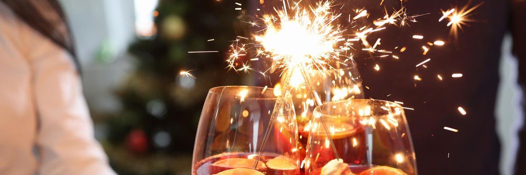 Three glasses with cocktails and sparklers on background of New Year tree. Christmas party concept