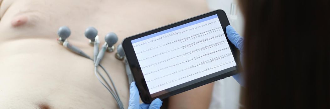 Doctor taking cardiogram to sick patient man on digital tablet in clinic closeup. Emergency cardiac care concept