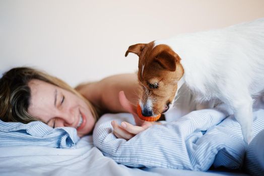 Woman lying in bed and playing with her dog, Lazy weekend, Morning relax