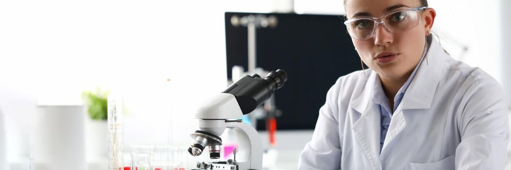 Woman scientist chemist sitting in front of microscope in laboratory. Chemical production of cosmetics concept