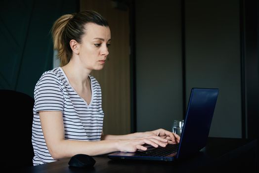 Caucasian woman sitting at table at home office and works with laptop. Freelancer remotely working