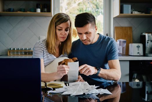Man and woman checking payment bills in the kitchen at home. Planning family budget. Couple calculate bills and have stress