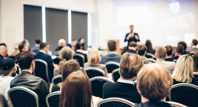 Speaker giving a talk in conference hall at business event. Rear view of unrecognizable people in audience at the conference hall. Business and entrepreneurship concept