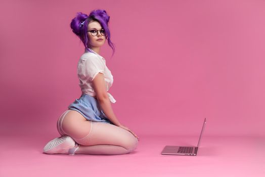 sexy girl with purple hair in summer clothes and beautiful underwear on a pink background with a laptop