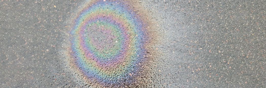 Rainbow stain on wet asphalt from machine oil closeup background. Environmental protection concept