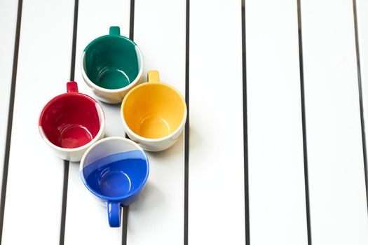 a small bowl-shaped container for drinking from, typically having a handle.Four cups on a white striped table.