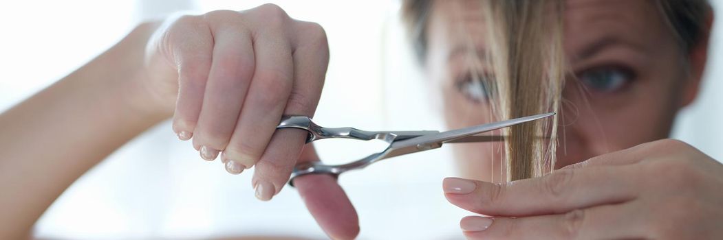 Young woman cutting off her bangs with scissors closeup. Life during lockdown concept