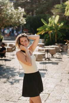 Girl tourist walking through ancient narrow street on a beautiful summer day in MEDITERRANEAN MEDIEVAL CITY , OLD TOWN bUDVA, MONTENEGRO. Young beautiful cheerful woman walking on old street at tropical town. Pretty girl looking at you and smiling