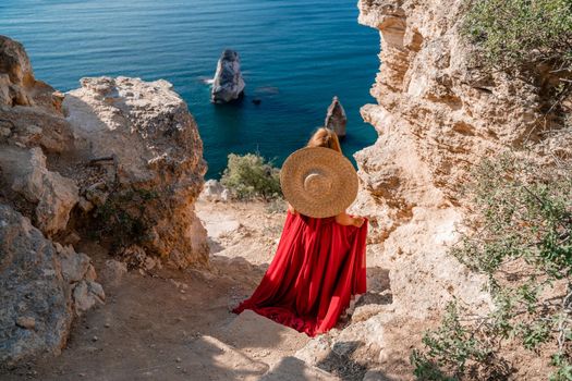 A woman in a flying red dress fluttering in the wind and a straw hat against the backdrop of the sea