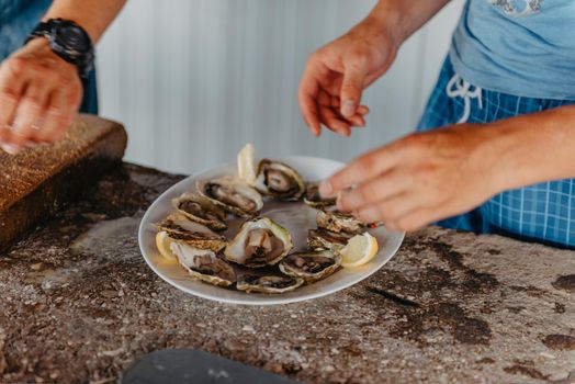 Fresh oysters with lime on a round plate. Oyster season. Macro-seafood dish. Oyster on the half shell.Two varieties of oysters.Out of focus. White plate of fresh oyster on ice and piece of lemon on wooden table