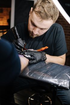 Tattoo master is tattooing a man's hand. Tattoo machine, safety and hygiene at work. Close-up of tattoo artist work. Tattoo salon.