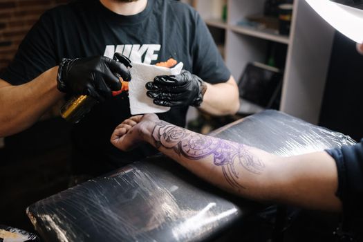 Close up of a young professional tattoo master introduces black ink into the skin using a needle from a tattoo machine. Tattoo on hand.