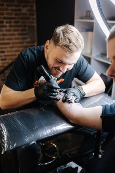 Tattoo master is tattooing a man's hand. Tattoo machine, safety and hygiene at work. Close-up of tattoo artist work. Tattoo salon.