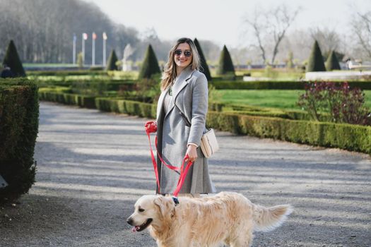 Stylish woman walking with a labrador on a leash in a park