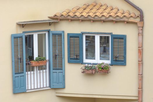Window and balcony with blue wooden shutters on light brown wall of building in Italy