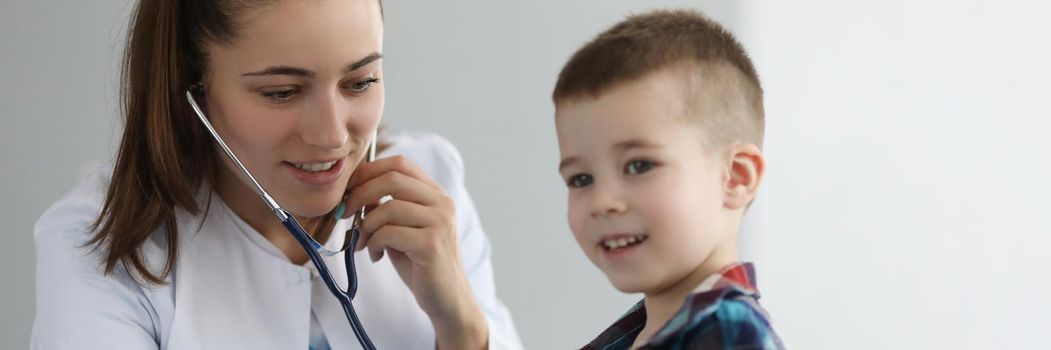 Doctor pediatrician listening to heart with stethoscope to little boy in clinic. Diagnosis of heart and lung disease in children concept