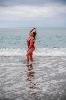 Woman in a bathing suit at the sea. A fat young woman in a red swimsuit enters the water during the surf.