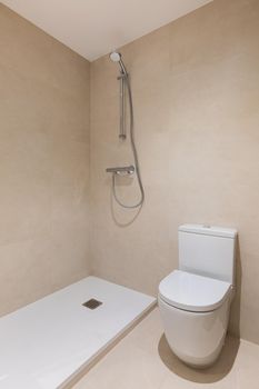 Bathroom with toilet, shower and ceramic tiled wall. Vertical view of modern minimalist interior.