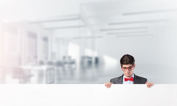 Young businessman holds a banner. Looks at the banner. Place for text