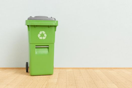 3D illustration of green recycling bin for trash placed on wooden floor against gray wall at home