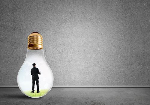 Businessman inside of light bulb in empty concrete room