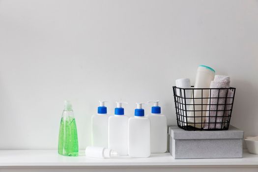 White bottles with a blue dispenser with shampoo, conditioner, cream and liquid soap are on a shelf in the bathroom. Green gel in a transparent bottle. Hand towels in an iron basket. Place for text.