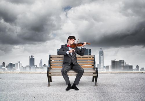 Young businessman plays the violin sitting on a wooden bench. Inspiration in business