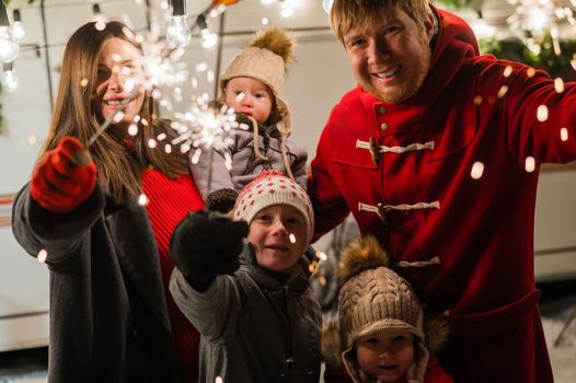 Happy large family celebrates christmas in nature and holds sparklers. Parents with three sons travels in a mobile home