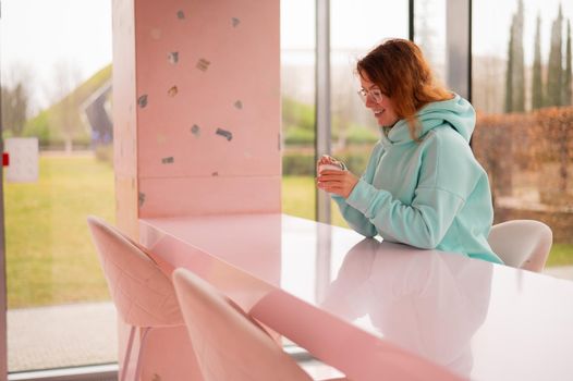 Caucasian red-haired woman eats ice cream with a plastic spoon while sitting alone in a cafe